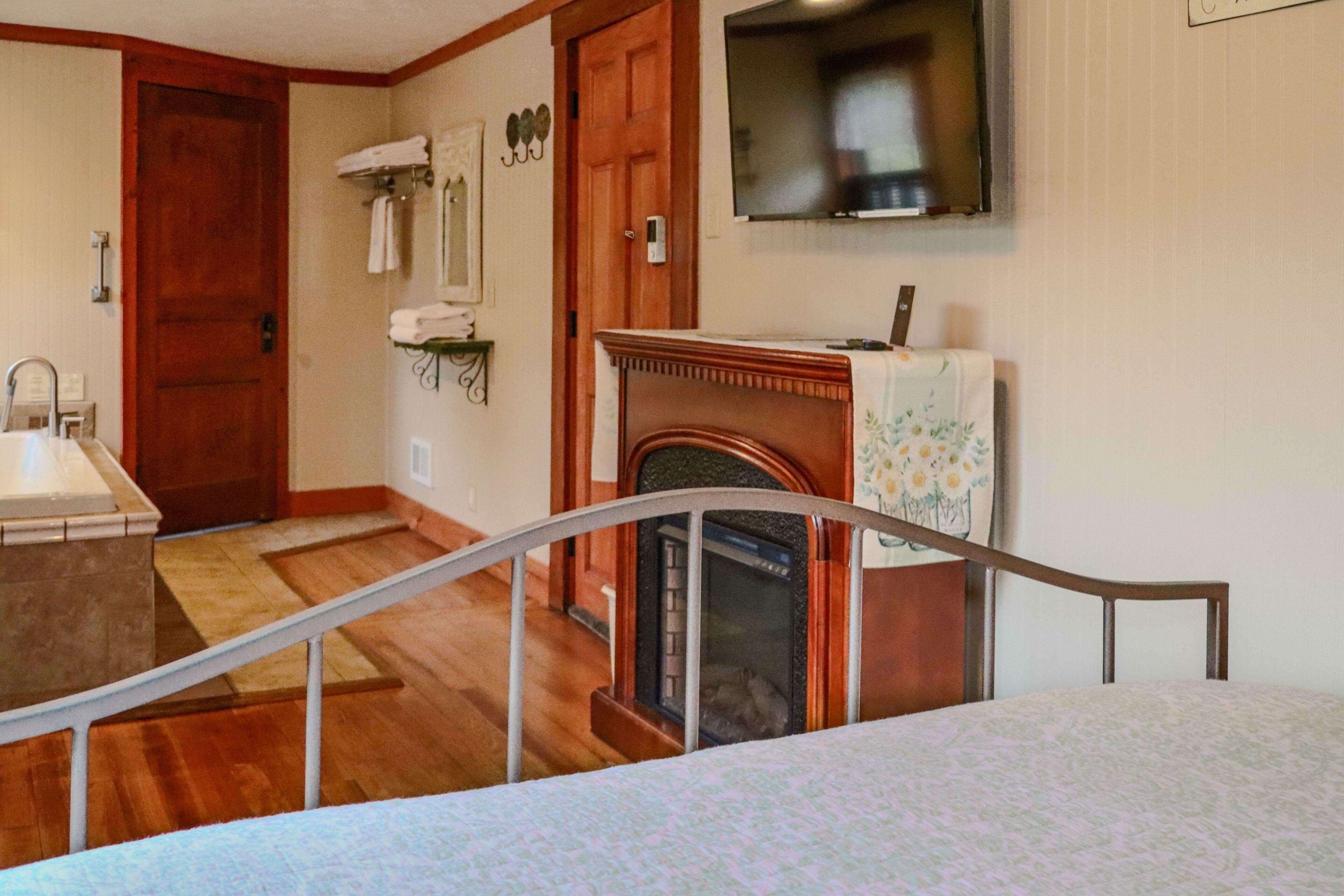 A room with a wooden floor, a fireplace, a television mounted on the wall, and a door leading to another room.