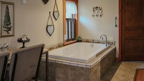 A bathroom with a bathtub, a vanity with a mirror, and a door. - Romantic Inn suite with Air Jet Jacuzzi & private bath (Logan)