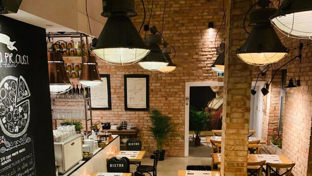 Ein gemütliches Bistro mit Backsteinwänden, Pendelleuchten und verschiedenen Sitzgelegenheiten, darunter Tische und Stühle.