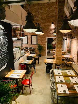 Un bistrot chaleureux aux murs de briques, doté d’un éclairage suspendu et offrant différents types de sièges, notamment des tables et des chaises.