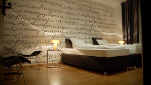 Ein Schlafzimmer mit einer großen Wand voller handgeschriebener Texte, einem Bett, Nachttischen, einem Sessel und einer Lampe.