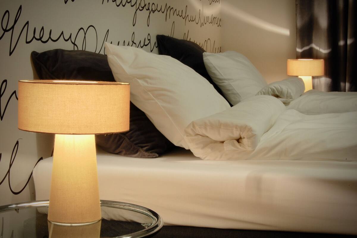 A neatly made bed with white linens and a lamp on a bedside table.