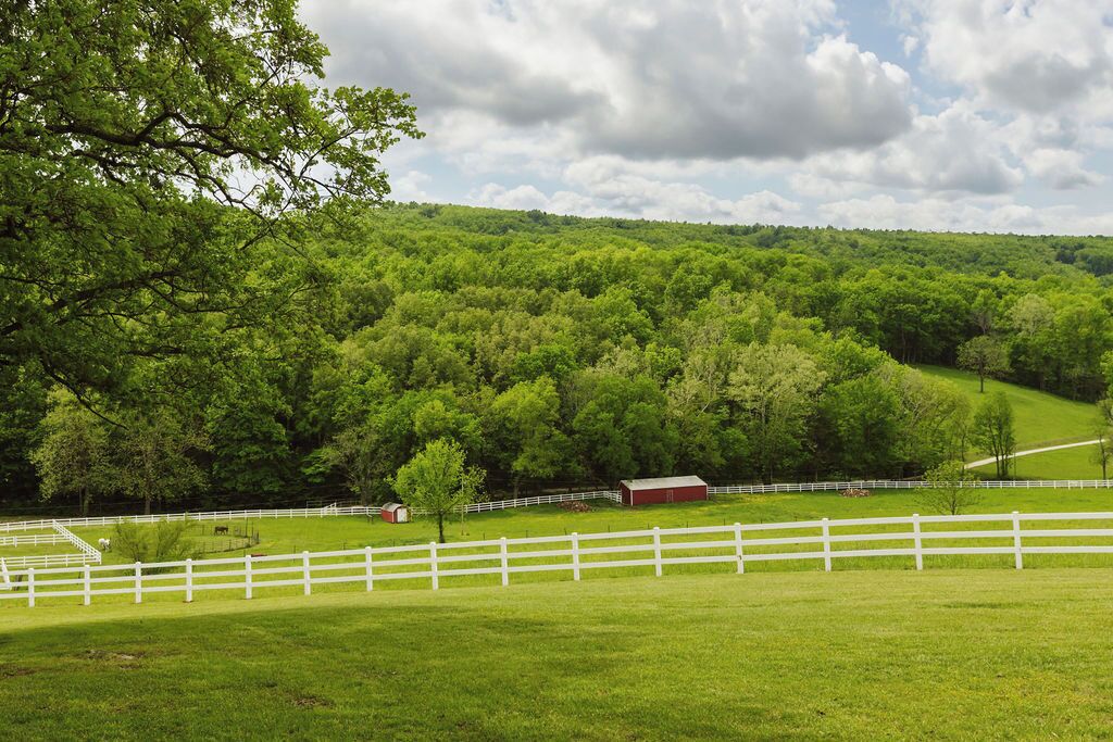 Un paysage rural avec une clôture blanche, des champs verdoyants et une grange rouge.