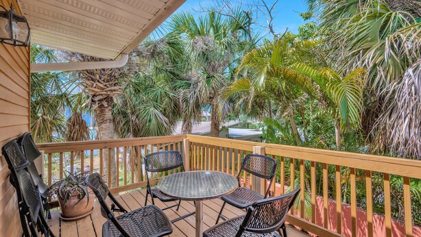 A wooden deck with a round table and four chairs, surrounded by lush tropical plants and palm trees. - Awesome Location! ☀Unlimited Sunsets Included☀ (Indian Rocks Beach)
