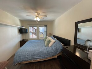 A bedroom with a bed, a ceiling fan, a TV, and a window with a view of a staircase. - Nothing beats Ocean Front (San Diego)