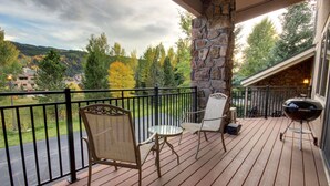Une terrasse en bois avec des sièges d’extérieur, un pilier en pierre et une vue sur un paysage montagneux.
