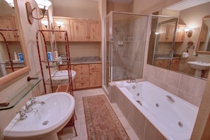 A bathroom with a glass shower enclosure, a large bathtub, and two sinks.