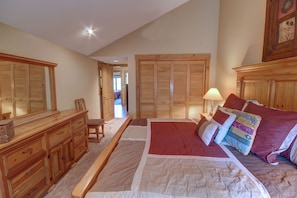 A bedroom with a large bed, wooden wardrobe, and a desk with drawers.