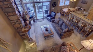 A spacious living room with a stone fireplace, a large couch, a coffee table, and a dining area with chairs and a table. - Northstar 1964 (Keystone)