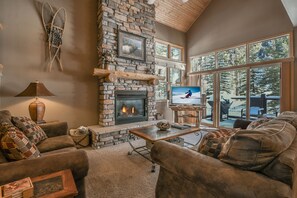 A cozy living room with a stone fireplace, comfortable seating, and large windows offering a view of the outdoors. - Northstar 1964 (Keystone)