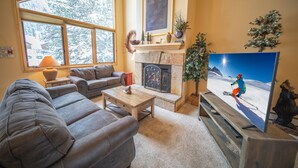 A cozy living room with a fireplace, a television, and a large window. - Ironwood 2986 by SummitCove Vacation Lodging (Keystone)