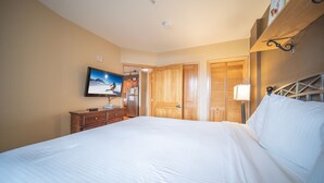 A hotel room with a large bed, wooden wardrobe, a television mounted on the wall, and a bedside table with a lamp. - Silver Mill 8283 (Keystone)