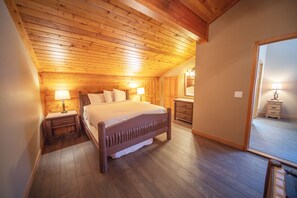 A bedroom with a wooden ceiling, a bed with white bedding, two bedside tables with lamps, and a dresser. - Ski Run 411 (Keystone)