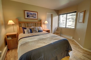 A bedroom with a large bed, two bedside tables, a chair, and a window with a view of trees. - Flying Dutchman 1164 by SummitCove Vacation Lodging (Keystone)