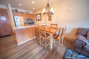 A kitchen with wooden cabinets, a stainless steel refrigerator, a microwave, and a dining area with a wooden table and chairs. - Springs 8864 (Keystone)