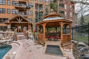 A wooden gazebo with a metal roof, surrounded by a pool area with steps leading to a building entrance. - Springs 8864 (Keystone)