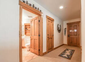 Un couloir avec des portes en bois, un sol recouvert de moquette et une salle de bain visible à travers une porte ouverte.