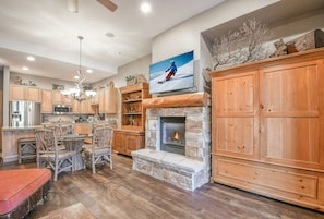 A spacious kitchen with a stone fireplace, wooden cabinets, and a dining area with chairs.