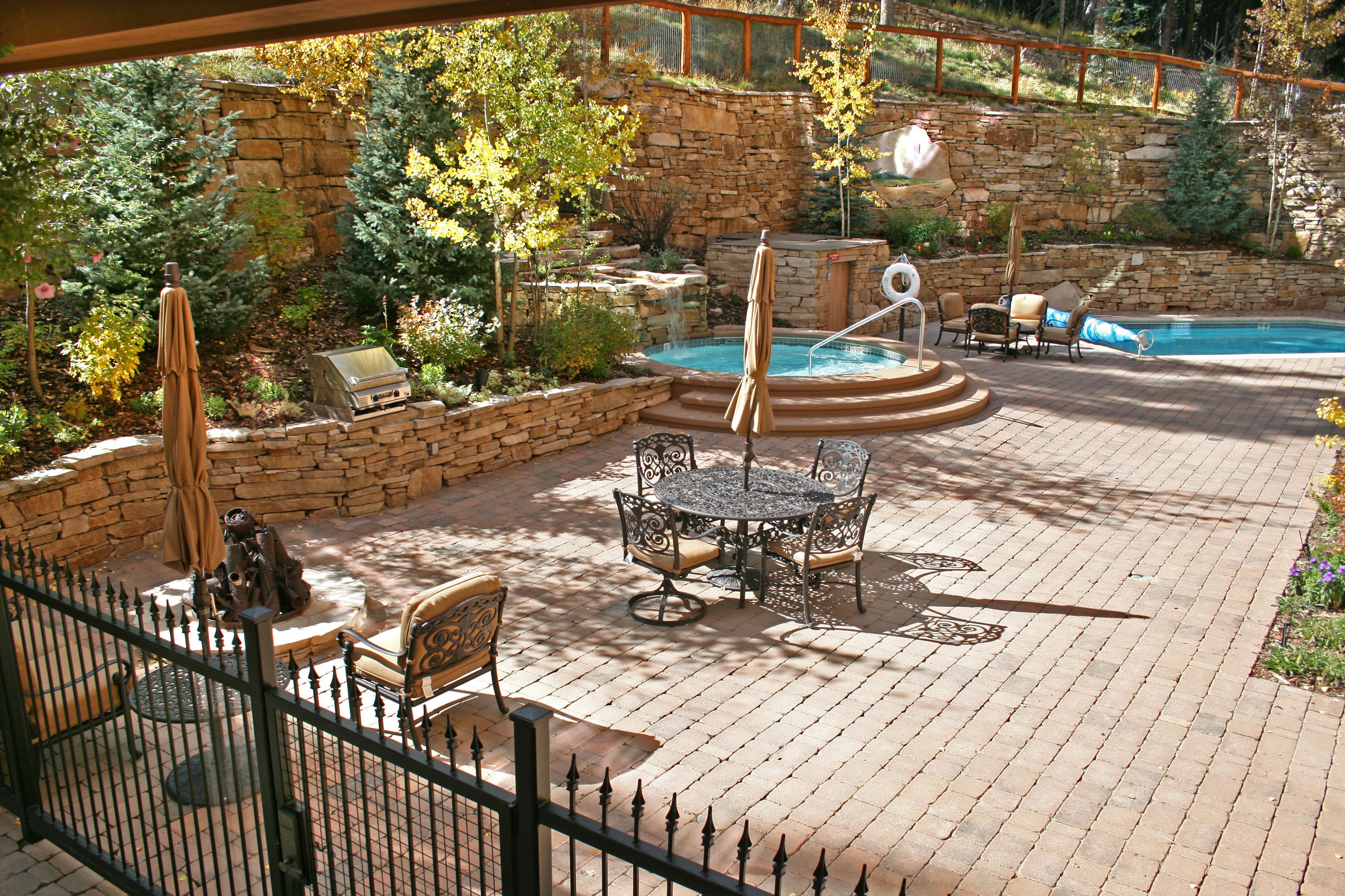 A backyard with a stone wall, a hot tub, a pool, and outdoor furniture.