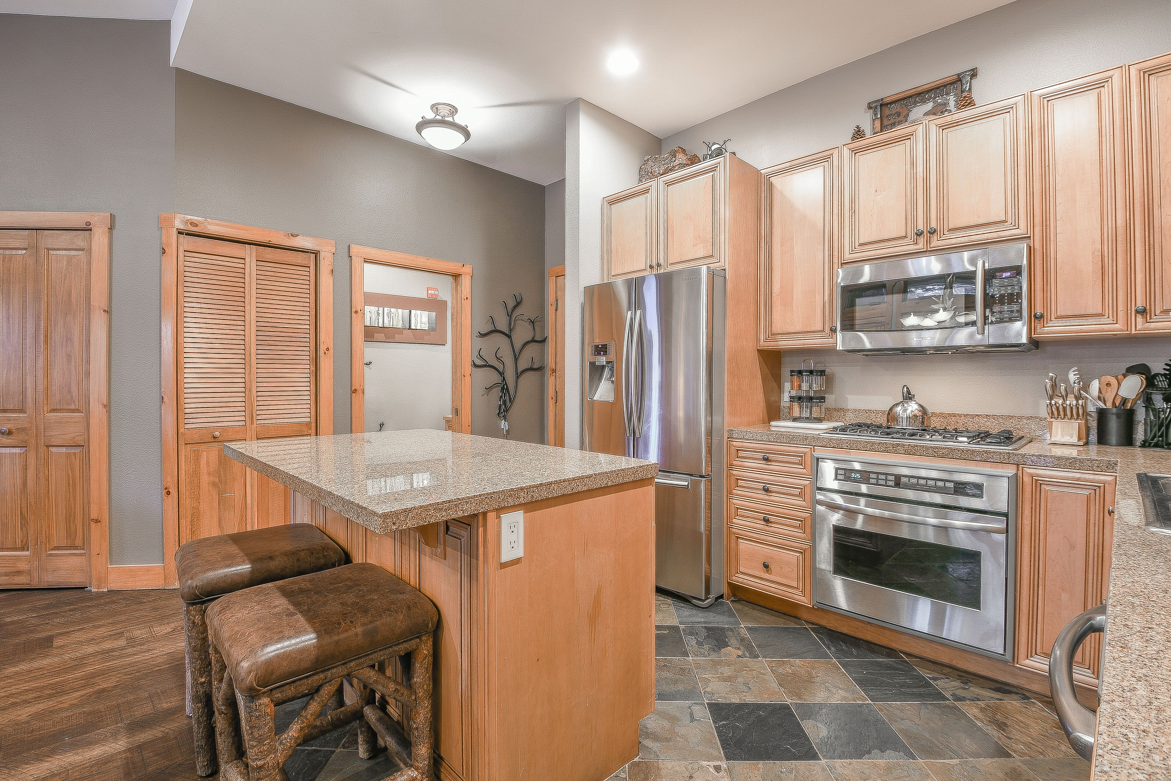 A kitchen with wooden cabinets, a stainless steel refrigerator, an oven, and a granite countertop.