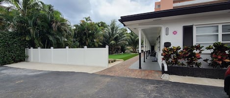 A modern building with a covered porch, a brick pathway, and lush greenery.
