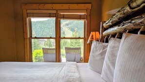 Ein Schlafzimmer mit einem großen Bett, einem Fenster mit Blick auf einen Wald und einem hölzernen Kopfteil.
