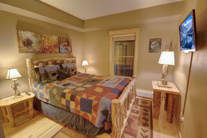 Relax in this serene bedroom with a large bed, nightstand, and chair, surrounded by framed artwork and a beautiful forest view.