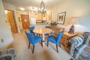Un espacio habitable compacto con una mesa de comedor rodeada de sillas azules, un sofá, un armario de madera y una araña.