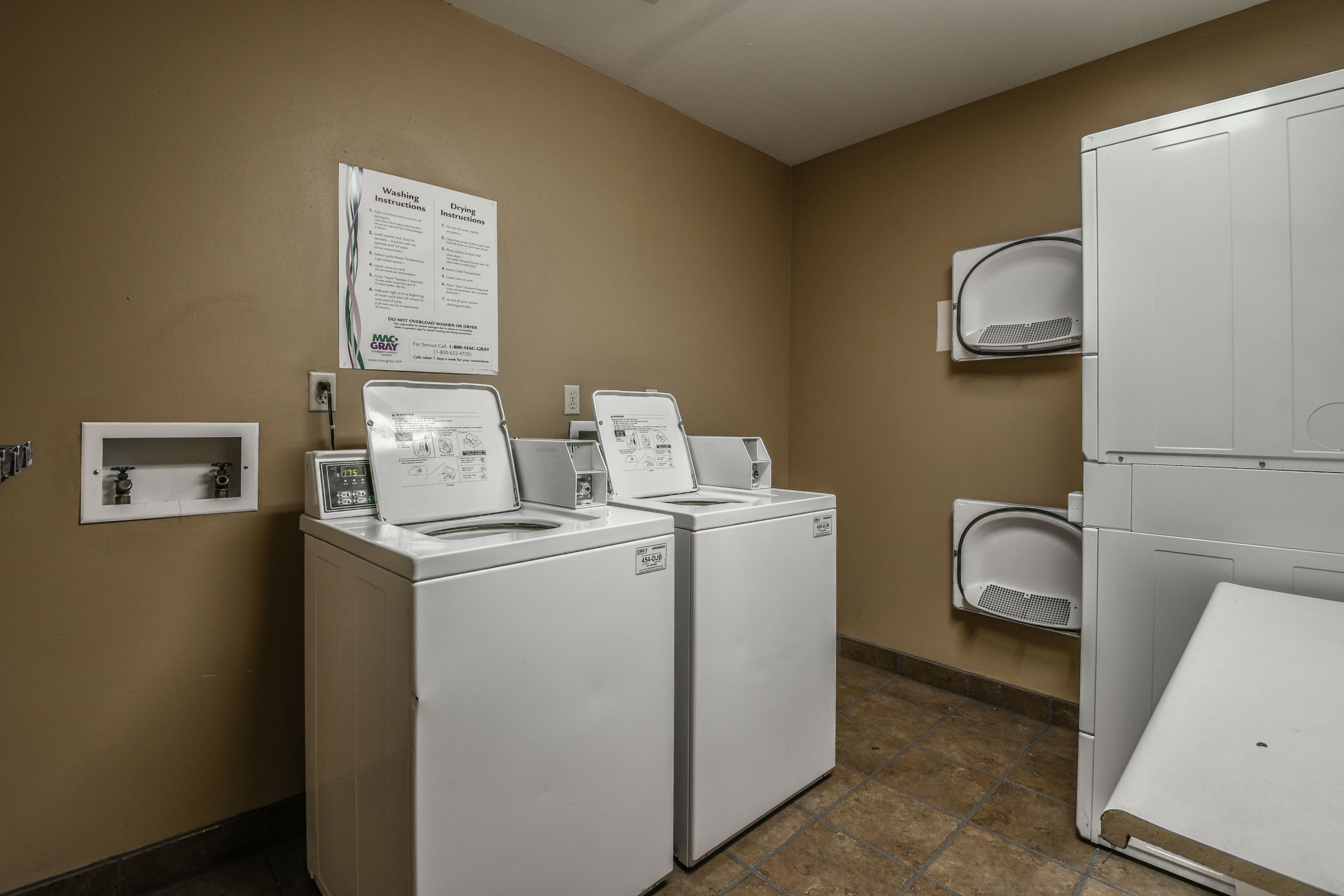 A laundry room with two front-loading washers and dryers, a wall-mounted drying rack, and a sign with washing instructions.