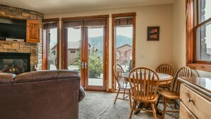 A cozy living room with a fireplace, a dining area with wooden chairs, and large glass doors leading to a scenic view.