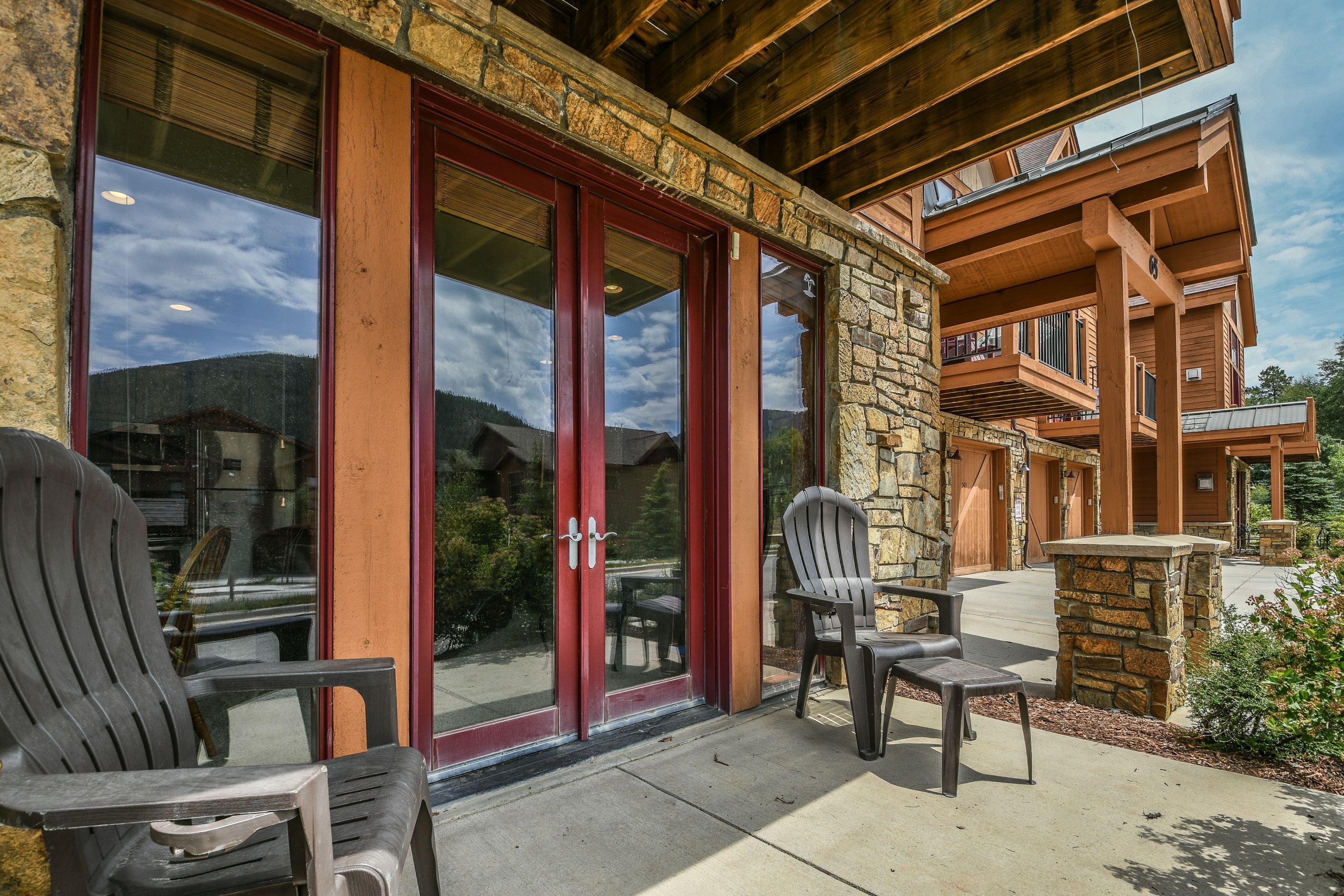 A lodge with a stone facade, large glass doors, and outdoor seating with Adirondack chairs.