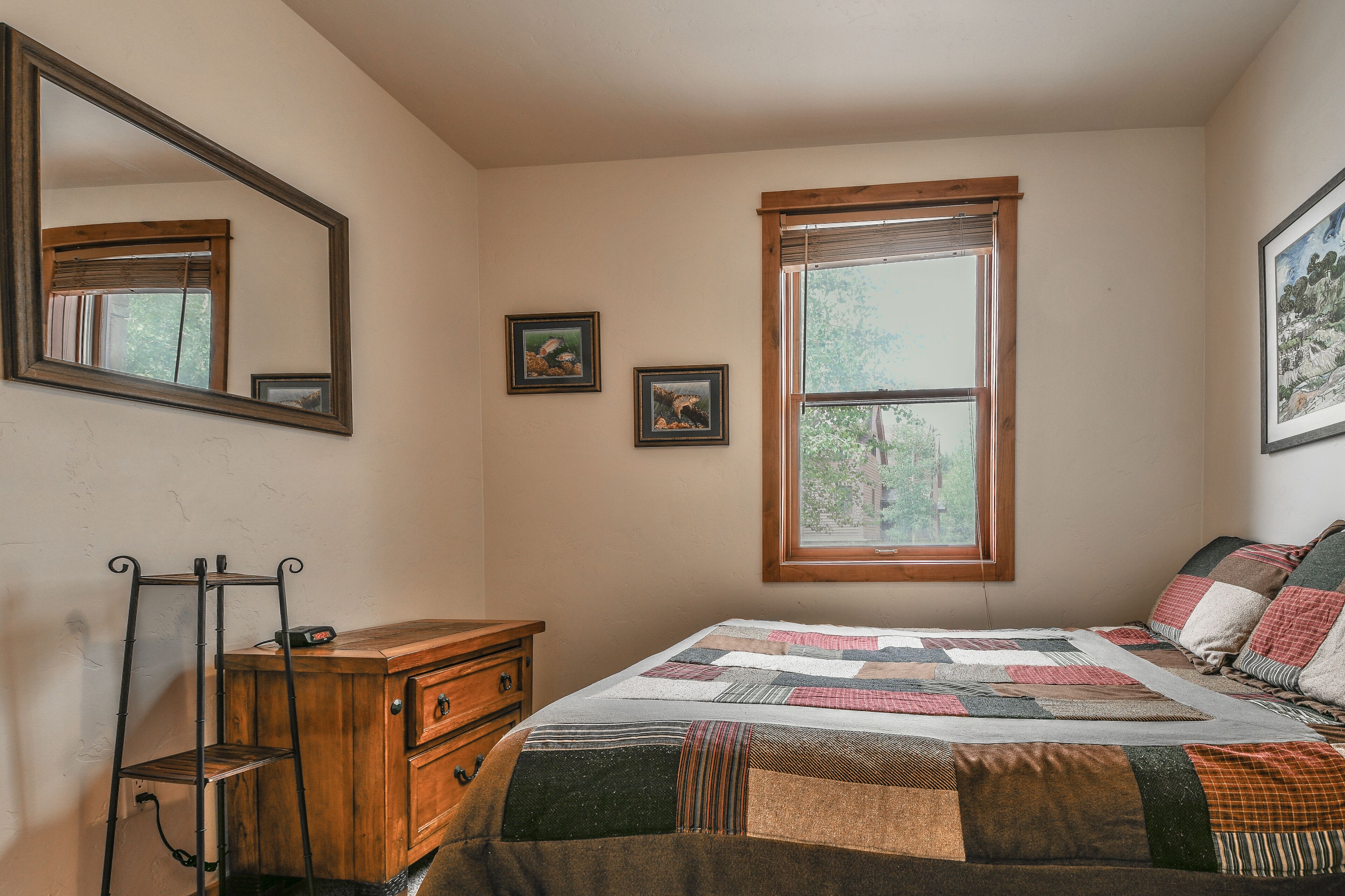 Une chambre à coucher avec une commode en bois, une couvre-lit matelassé, un miroir et une fenêtre donnant sur des arbres.