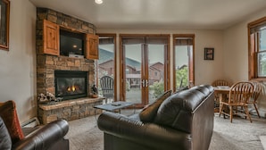 A cozy living room with a stone fireplace, leather sofa, and a dining area with wooden chairs.