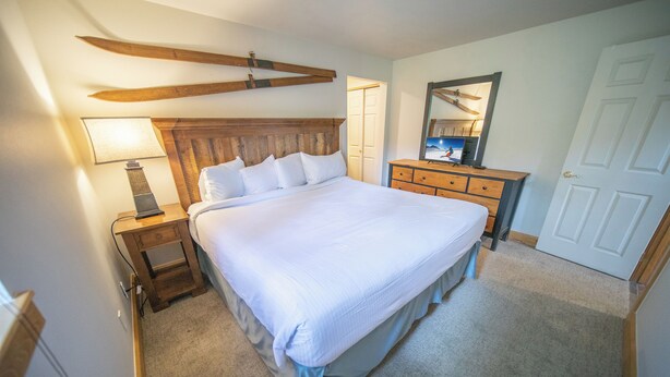 A bedroom with a large bed, wooden headboard, bedside table with lamp, dresser, and a mirror. - Starfire 1979 (Keystone)