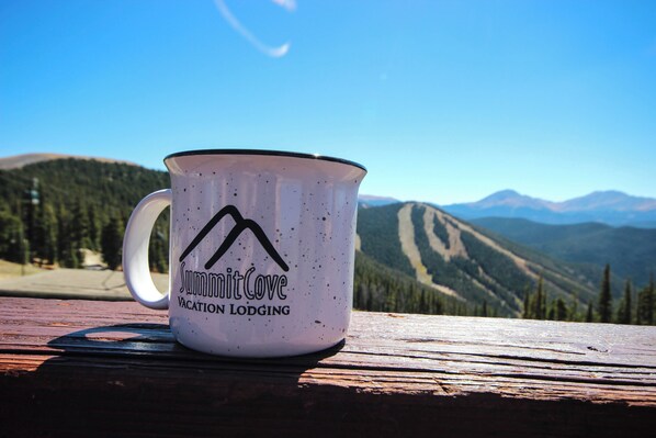 A white mug with "SummitCove Vacation Lodging" text and a mountain logo on a wooden surface with a mountain view in the background.