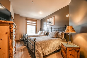 A bedroom with two beds, a wooden dresser, a television, and a window with blinds.
