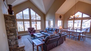 A spacious living room with a stone fireplace, leather sofa, and a dining area with wooden chairs and a table. - Gateway Lodge 5036 by SummitCove Vacation Lodging (Keystone)