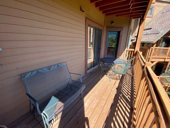 A wooden deck with a metal bench and a table, a wooden railing, and a door leading to a balcony. - Tenderfoot Lodge 2643 (Keystone)