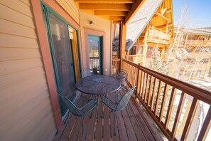 A wooden deck with a round table and chairs, a door, and a view of a snowy landscape. - Tenderfoot Lodge 2643 (Keystone)