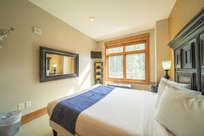 A neatly arranged bedroom with a large bed, a mirror, a window with a view of trees, and a bookshelf. - Lone Eagle 3034 by SummitCove Vacation Lodging (Keystone)