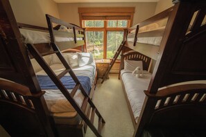 A room with bunk beds, a window with a view of trees, and a small table with a lamp. - Lone Eagle 3034 by SummitCove Vacation Lodging (Keystone)