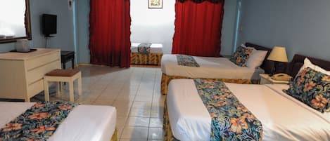 A hotel room with two beds, a desk, a chair, a TV, and a window with red curtains.