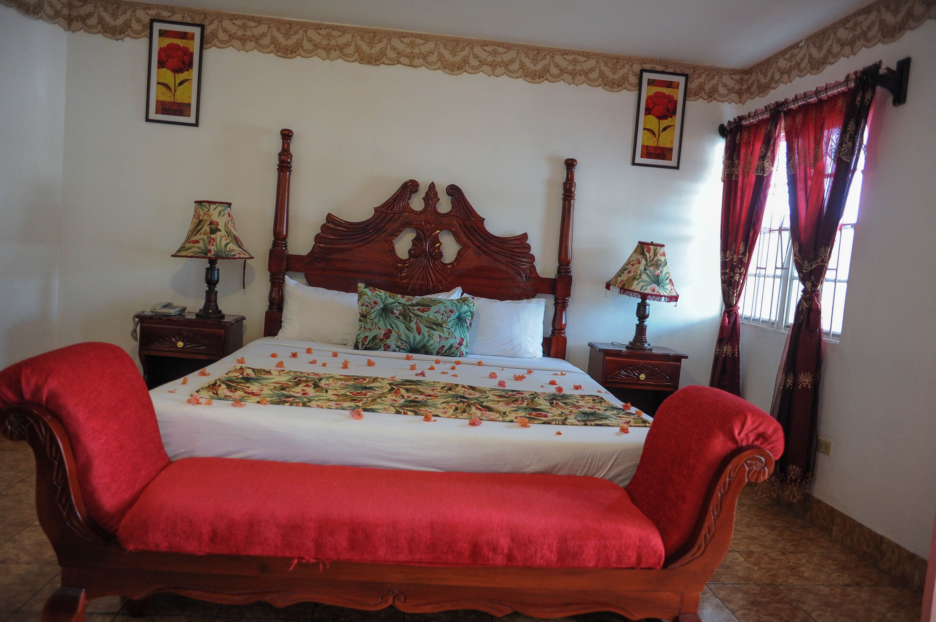 Un dormitorio con una cama grande, dos mesitas de noche, un banco rojo y una ventana con cortinas rojas.