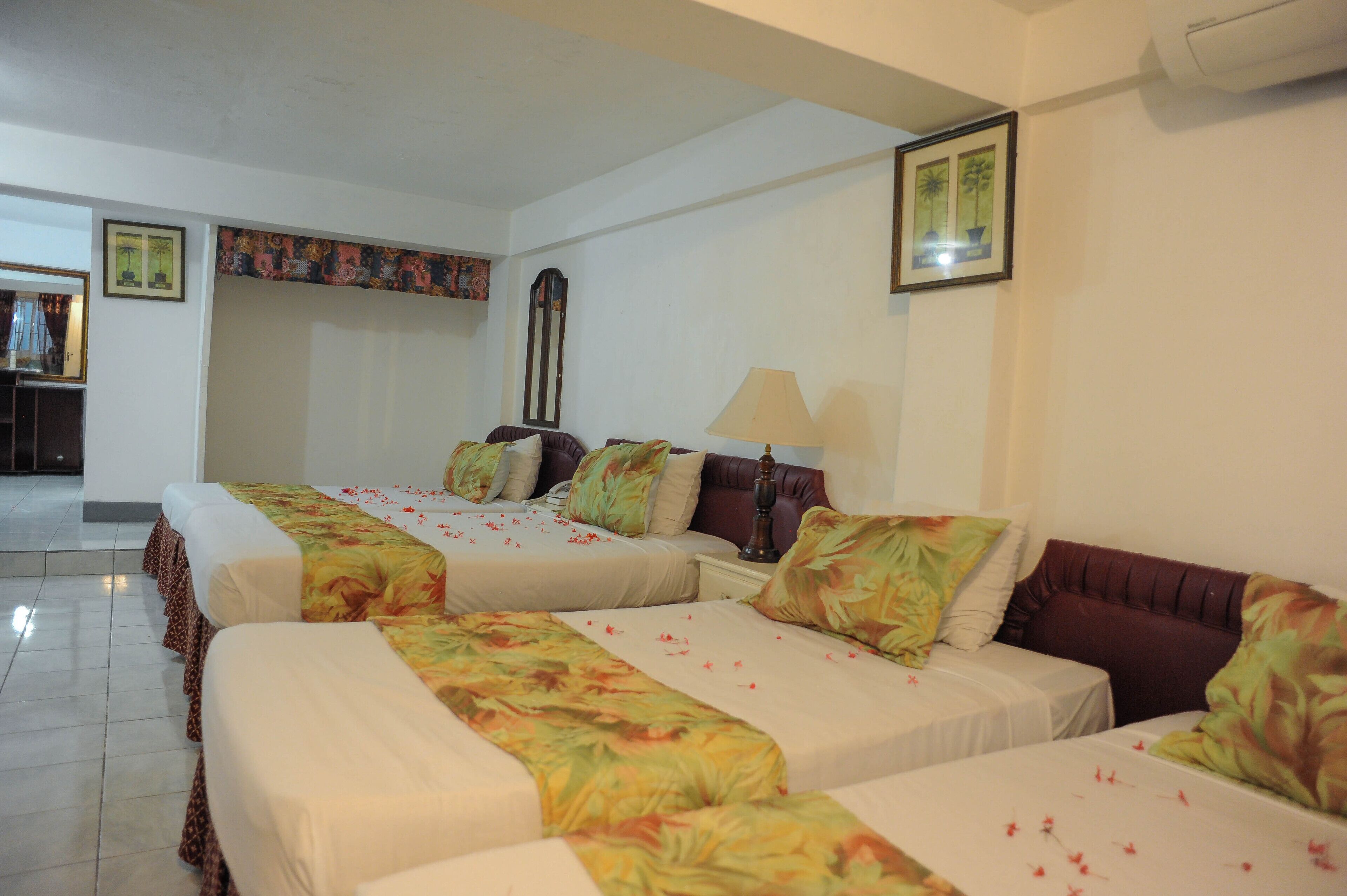 Habitación de hotel con cuatro camas individuales, un espejo grande y una lámpara fijada a la pared.