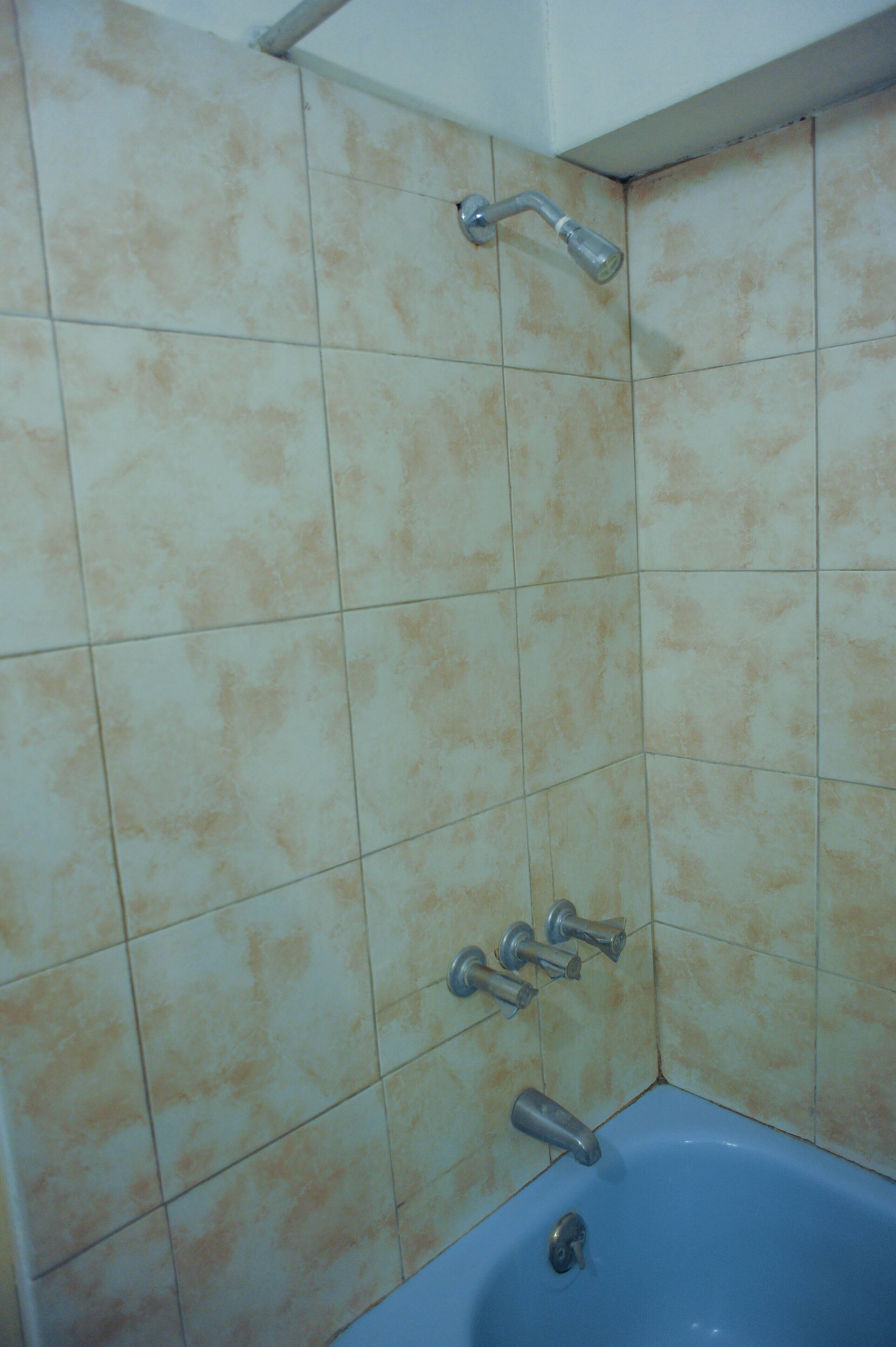 A bathroom with beige tiles, a blue bathtub, and two showerheads.