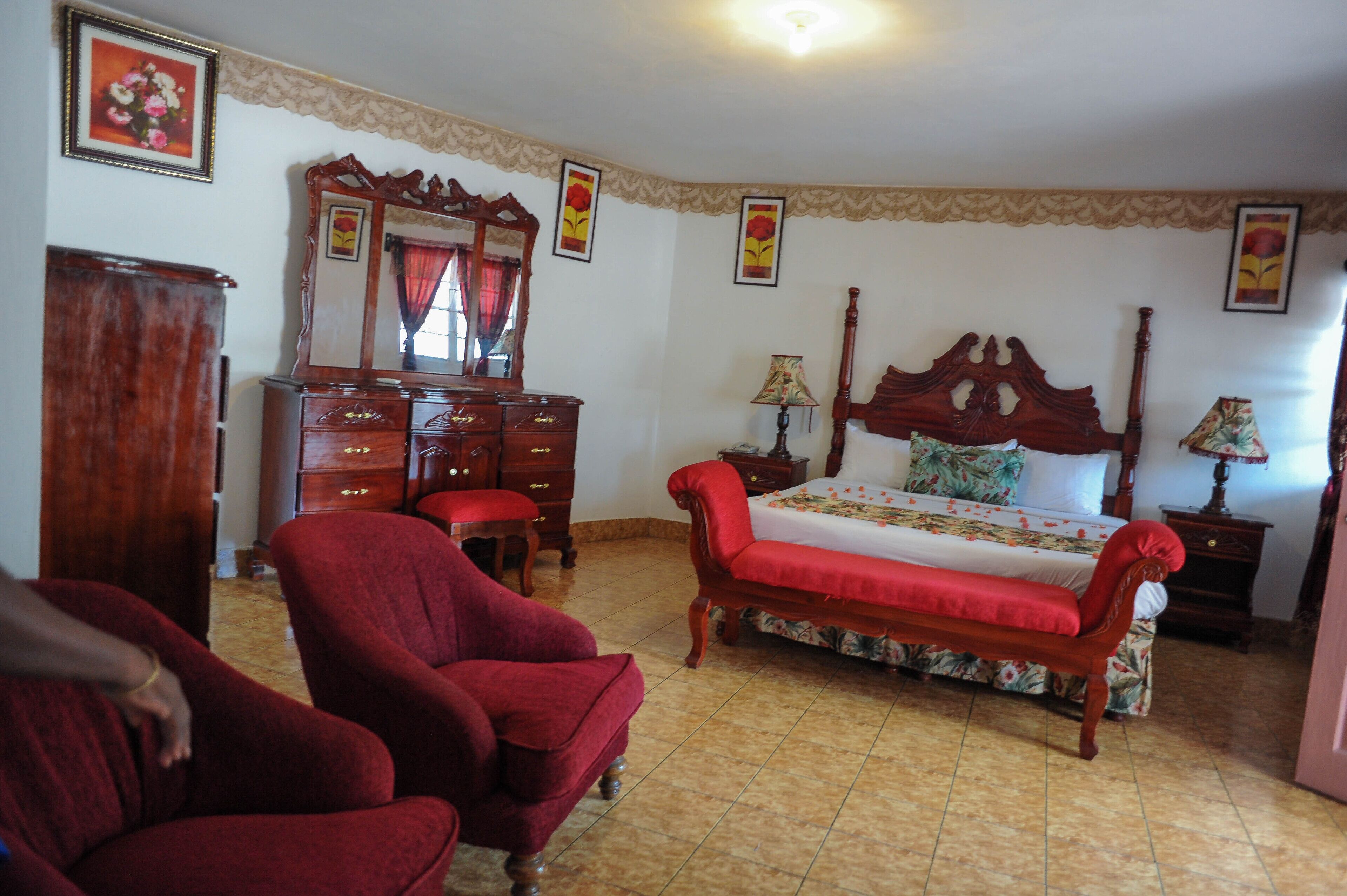A bedroom with a wooden bed, a dresser, a red armchair, and a mirror.