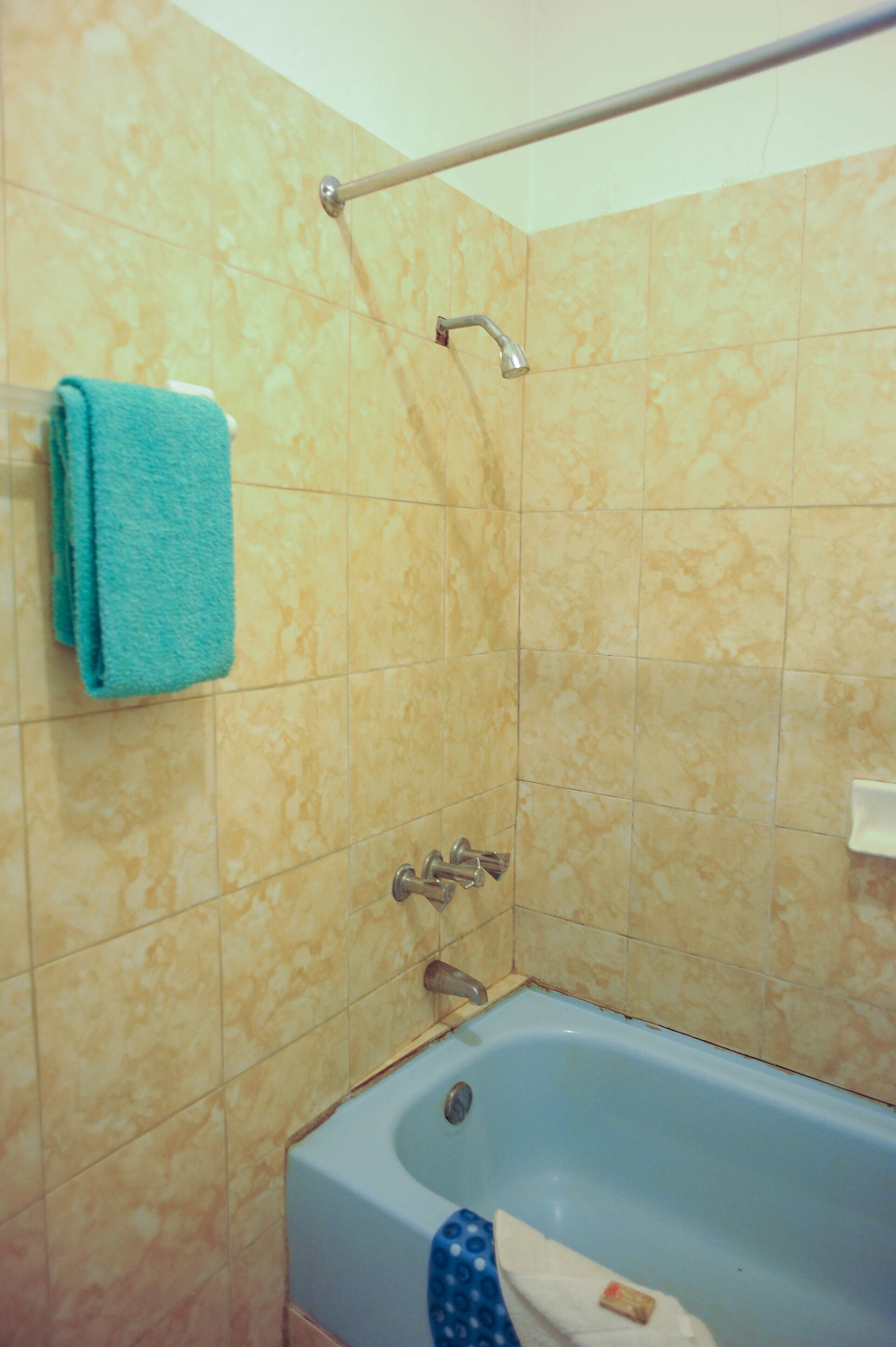 Un baño con bañera, un perchero con una toalla azul y un cabezal de ducha.
