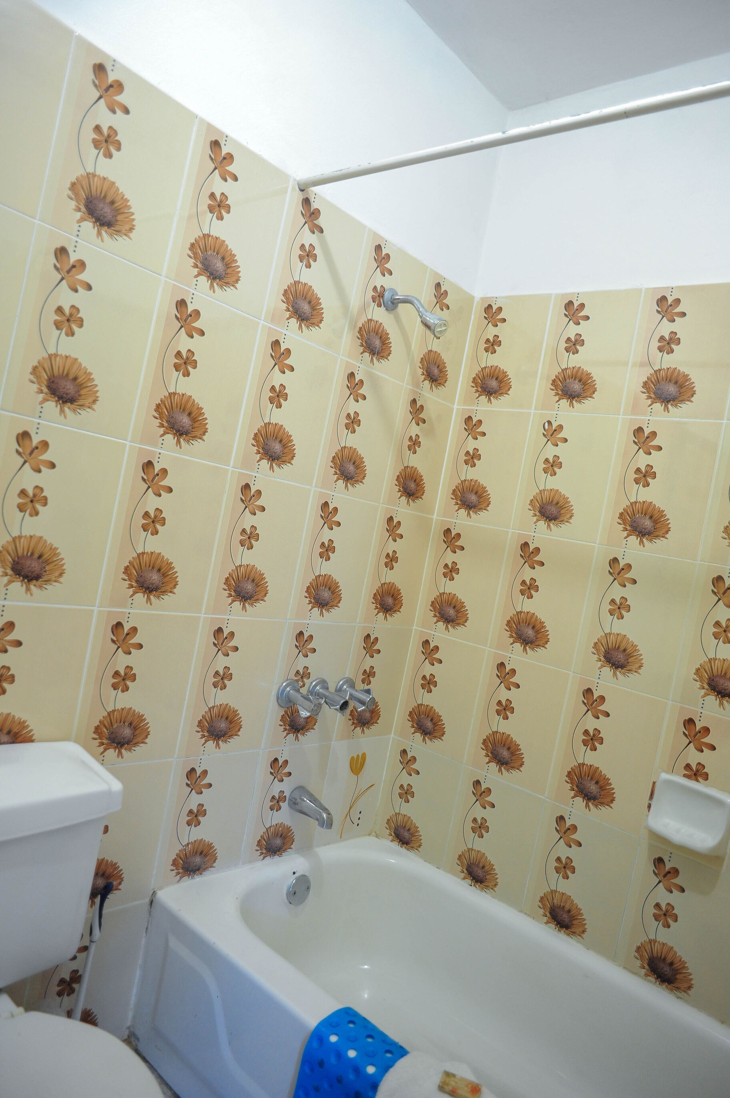 Et badeværelse med et blomstret flisemønster, et badekar, et toilet og en bruseniche.