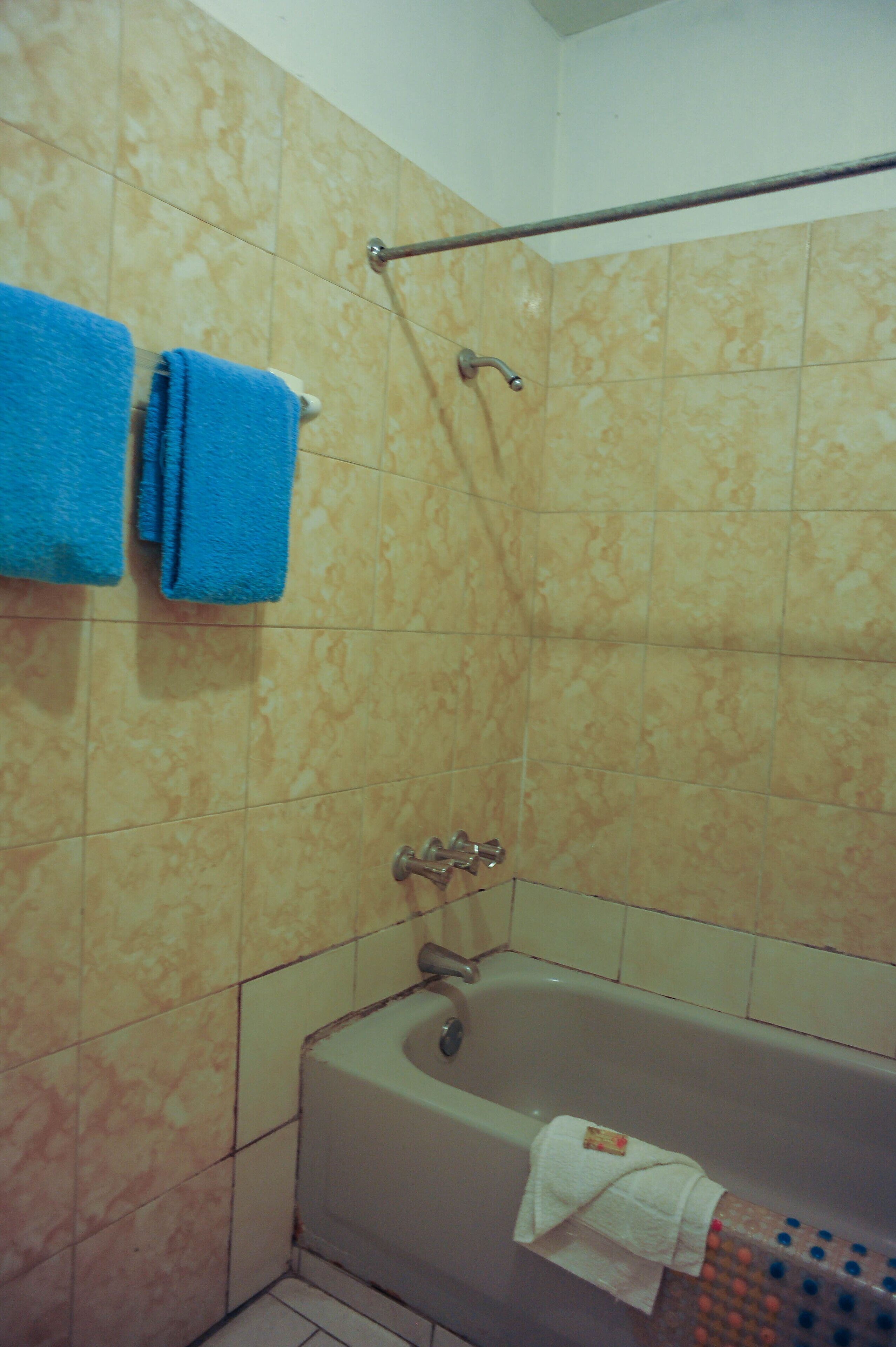 A bathroom with beige tiles, a bathtub, a showerhead, and two towels hanging on a rack.