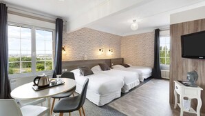 A hotel room with two beds, a dining table, chairs, a TV, and a view of greenery.